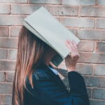 本で顔を覆って思考する女性